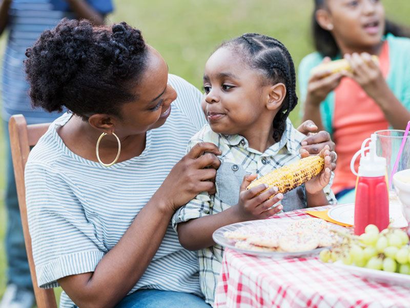 Mother And Son Smiling And Eating Roasted Corn On The Cob